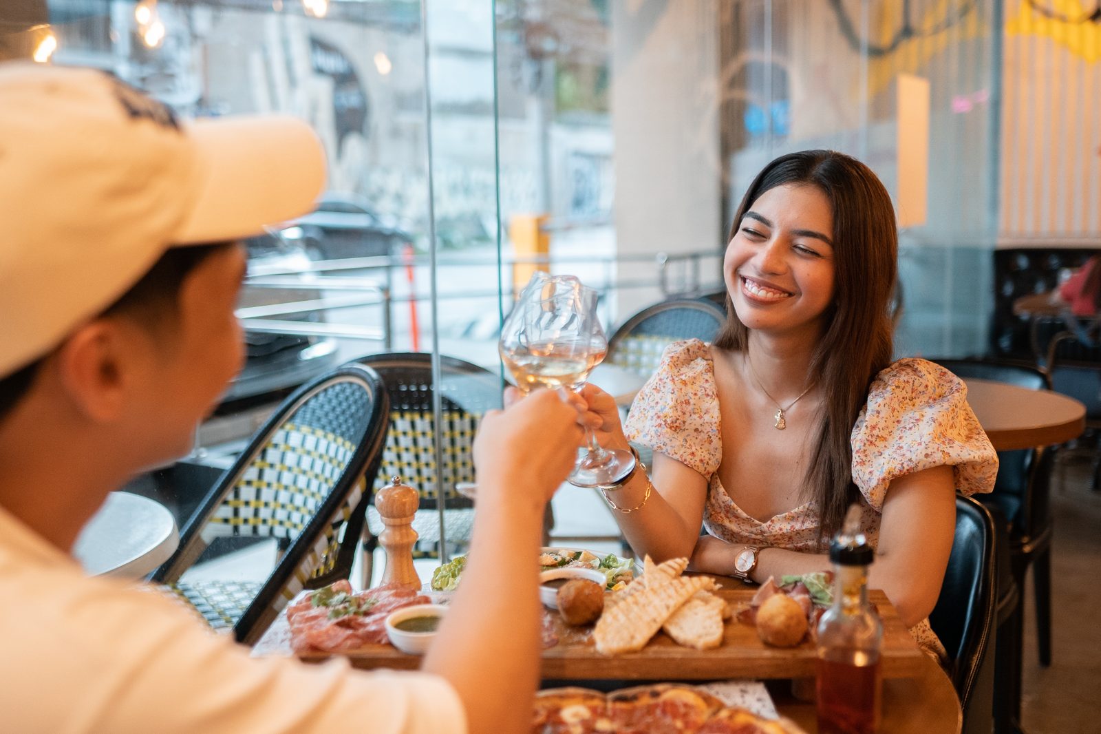 Two friends toasting with white wine over a charcuterie board and pizza at Napolitani